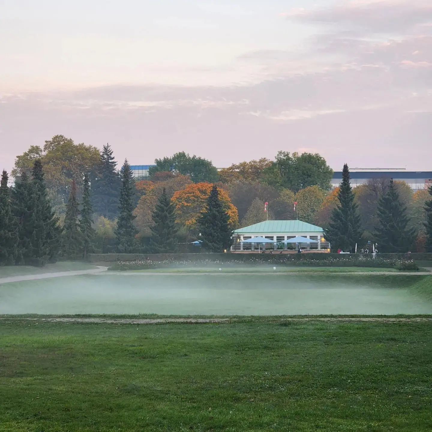 Mist drifting over a palace garden lawn bordered by autumn trees.