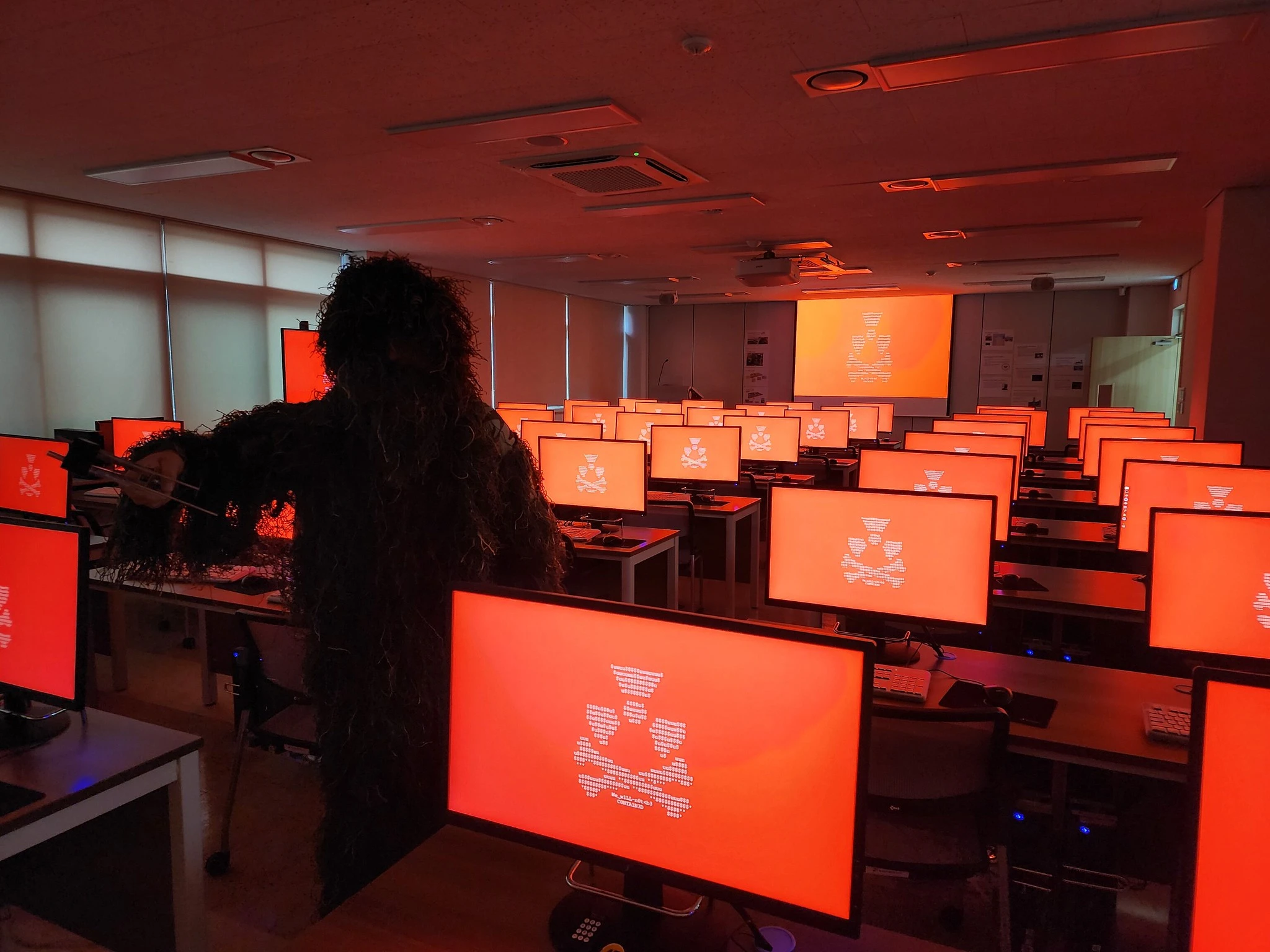 A figure in a ghillie suit stands among rows of computers glowing red with RLF propaganda.