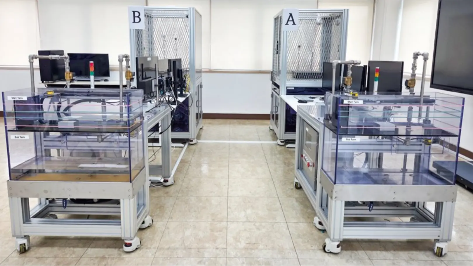 Two transparent spent-fuel-pool rigs with pumps, pipework, and control screens stand in front of two mesh-enclosed physical-protection rigs, arranged as paired A and B stations.